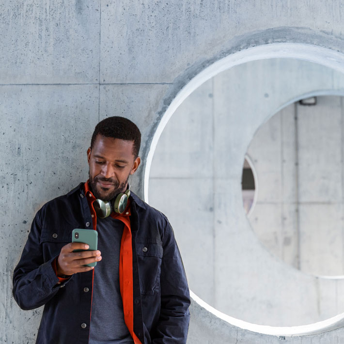 Person som lutar sig mot vägg och tittar ner i sin mobiltelefon.
