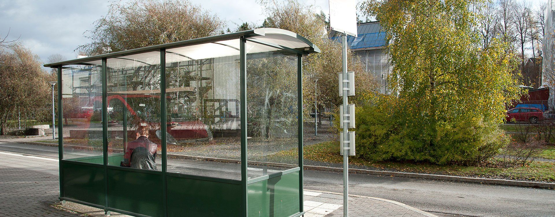 Ung kvinna väntar på bussen med flerbostadshus som byggs om i bakgrunden