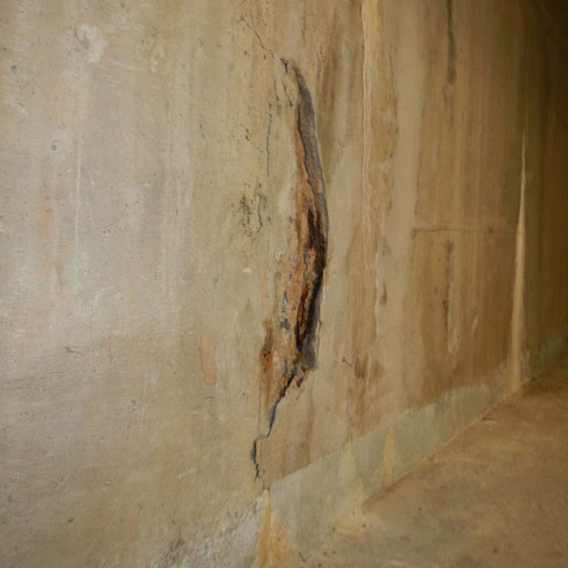 Betongvägg krackelerar och blottlägger rost.