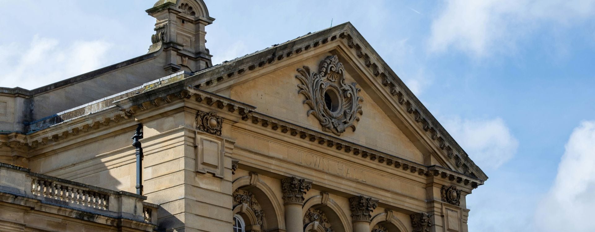 A picture of the face of Cheltenham Town Hall in Gloucestershire in the UK. The town hall is designed in classical style with three bays and three Corinthian columns on both the first and second storey, the frontage has a large decorative pediment at the top