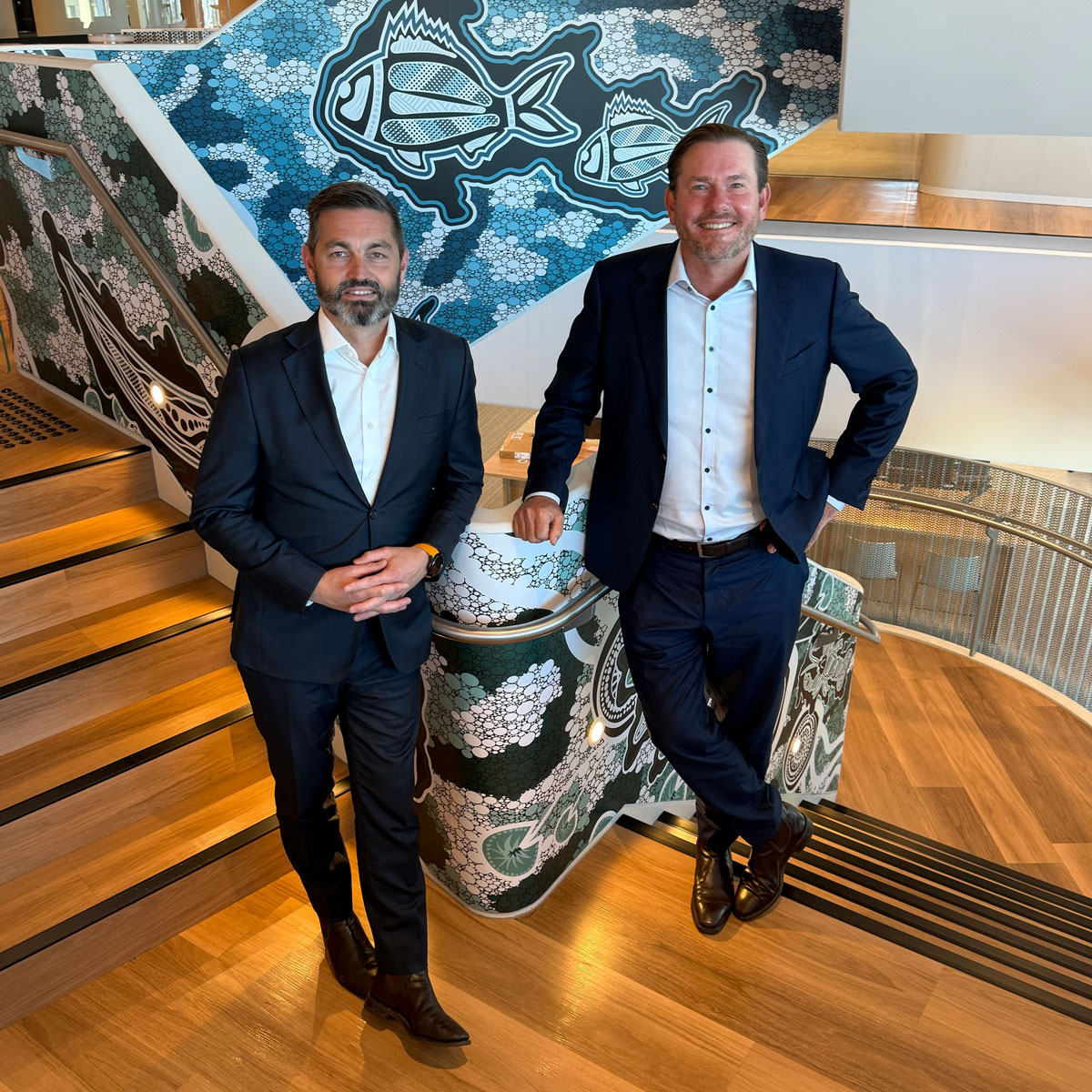 Greg Kane and Tom Hasker standing on stairs of WSP office with Indigenous art in the background
