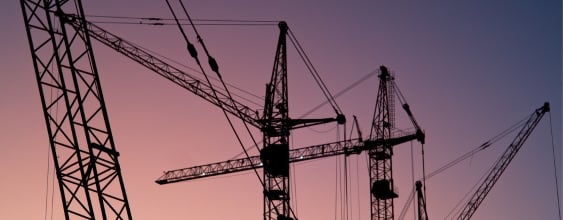 Construction cranes against a sunset