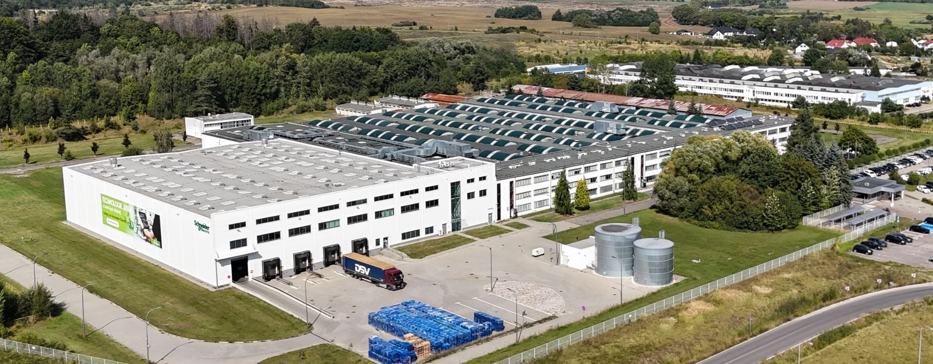 Aerial view of a large manufacturing and distribution facility surrounded by trees, roads, and industrial buildings.