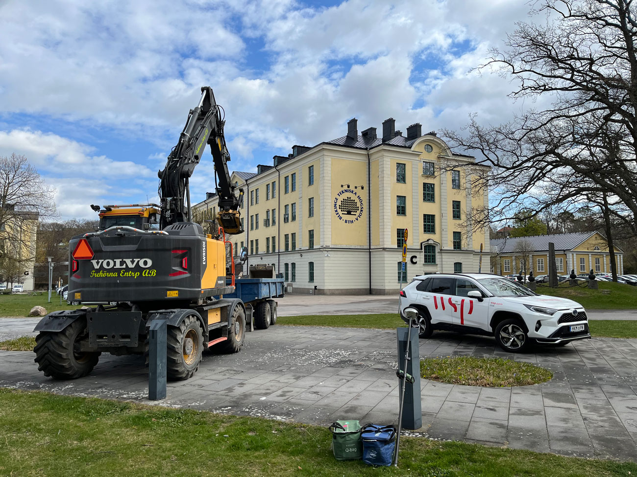 Grävmaskin och vit bil med wsp-logga på ett trog i Gräsvik.